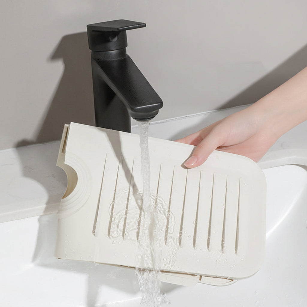 Off-white silicone faucet mat being rinsed under running water in a kitchen sink
