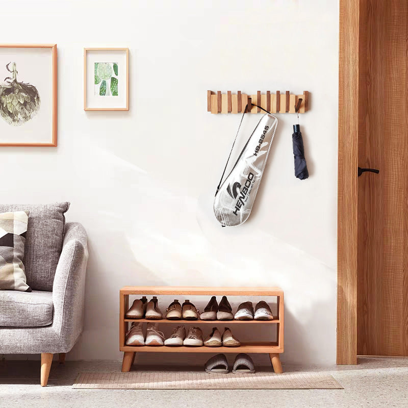 Wooden wall mounted folding coat rack holding a bag and umbrella above an entryway shoe rack
